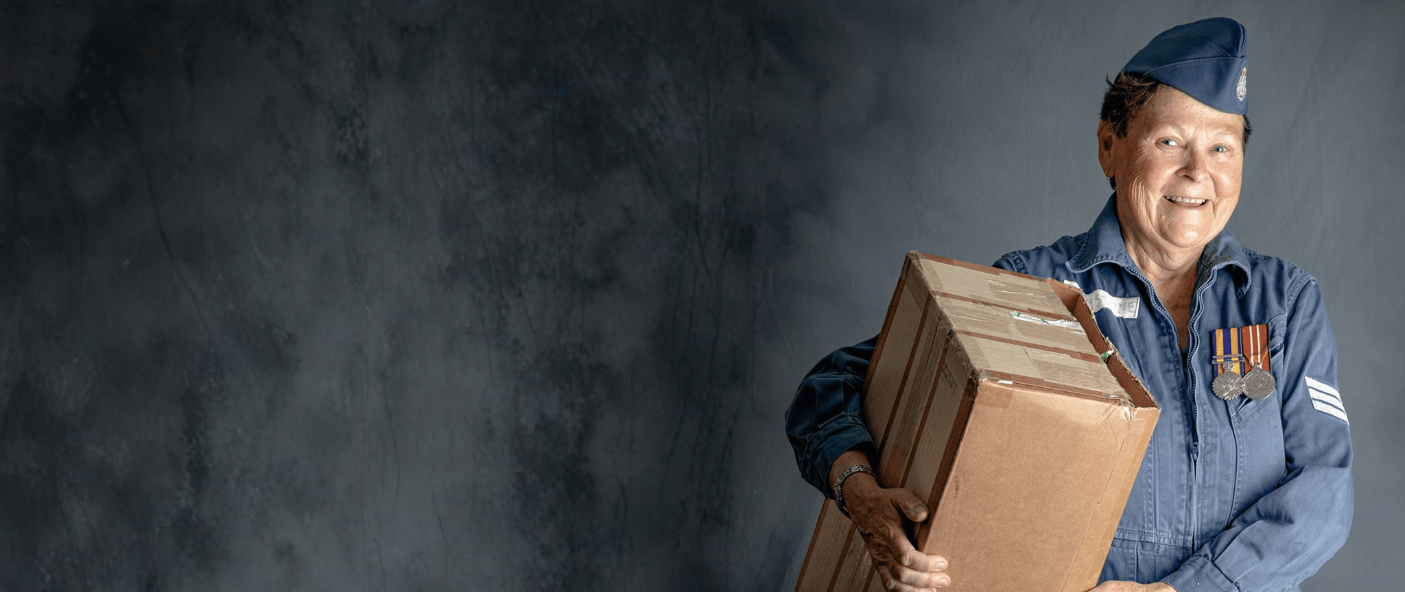 A veteran wears her medals and old uniform, carrying a box.