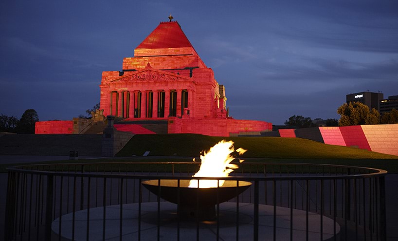 The Shrine of Remembrance is lit up with red lighting, with the Eternal Flame in the foreground