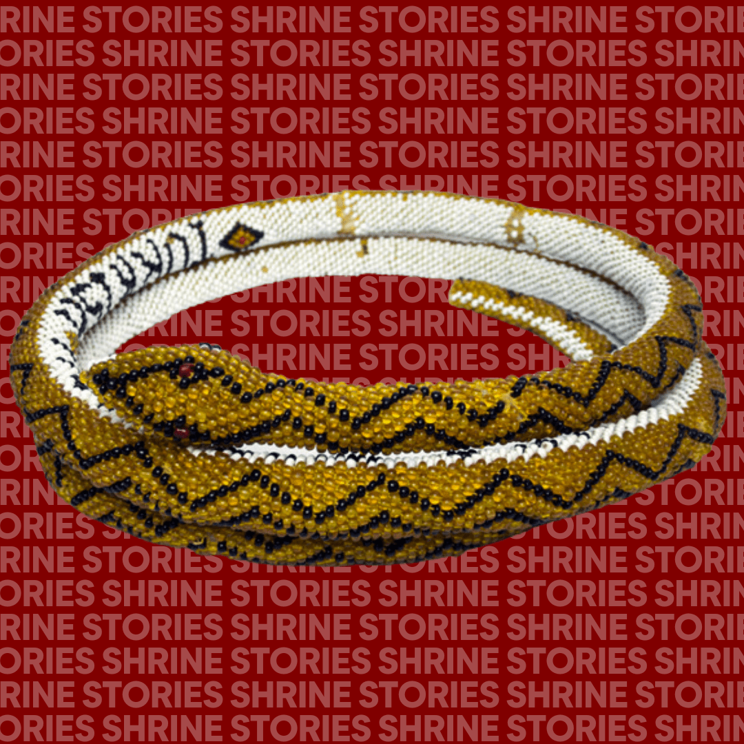 A black, white and yellow beaded snake coiled up in a circle. The snake says 'Turkish Prisoner of War' on it's belly. It has black zig zags that run along it's back, and red beaded eyes. 