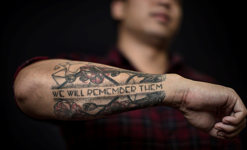 A person displaying their tattooed arm reading We Will Remember Them