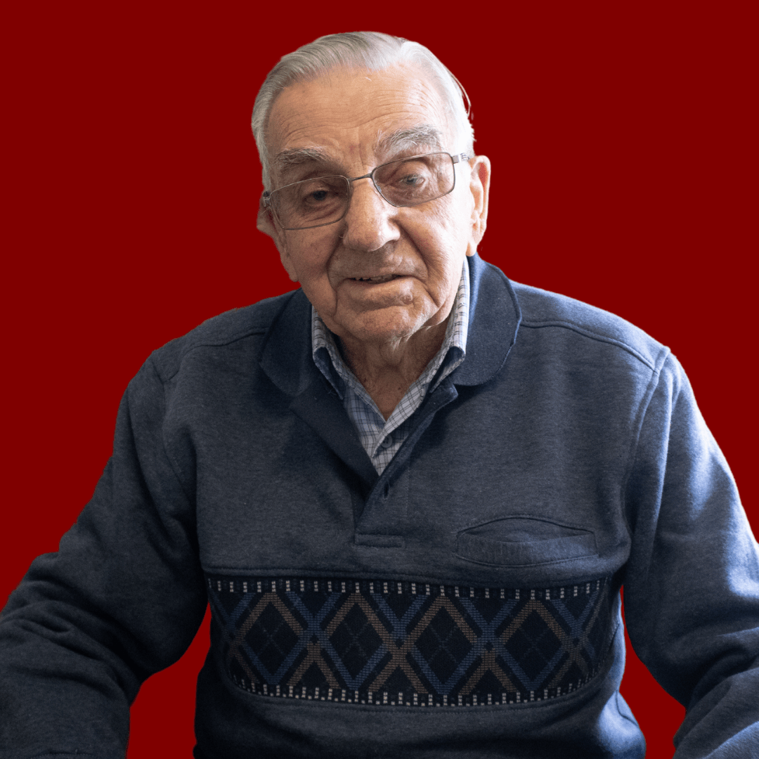 Vern Roberts wearing a blue jumper and glasses, smiling at the camera. 