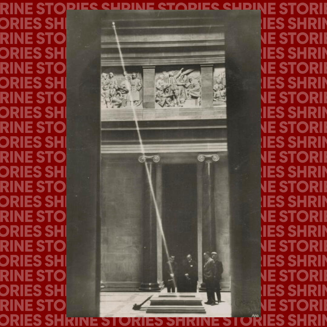 A historic black-and-white photo of sunlight beaming through a small opening onto a stone structure inside the Shrine of Remembrance. Several people stand in the background observing the sunlight. The image features intricate carvings above the entrance columns