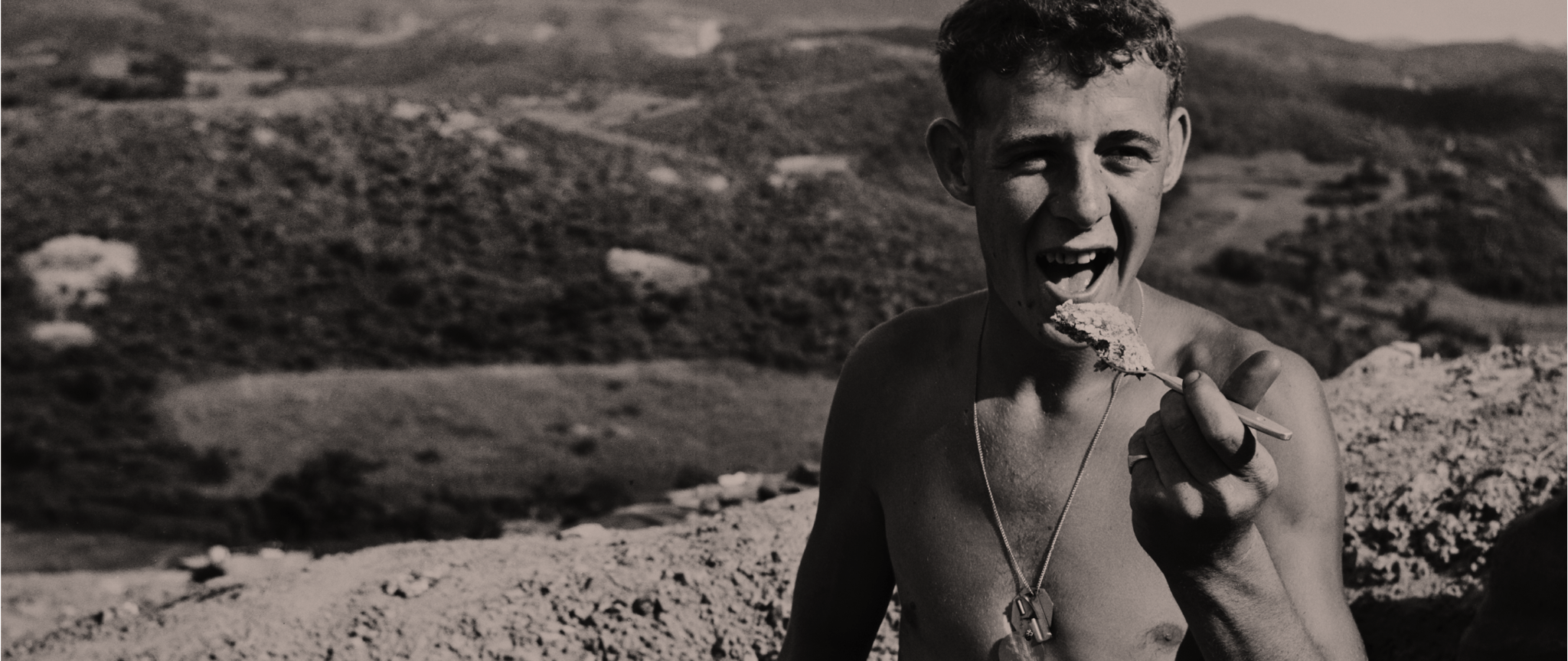 A shirtless soldier eats on duty