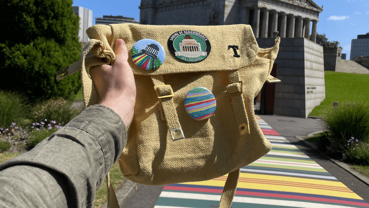 A bag with colourful badges is held in front of the Shrine of Remembrance